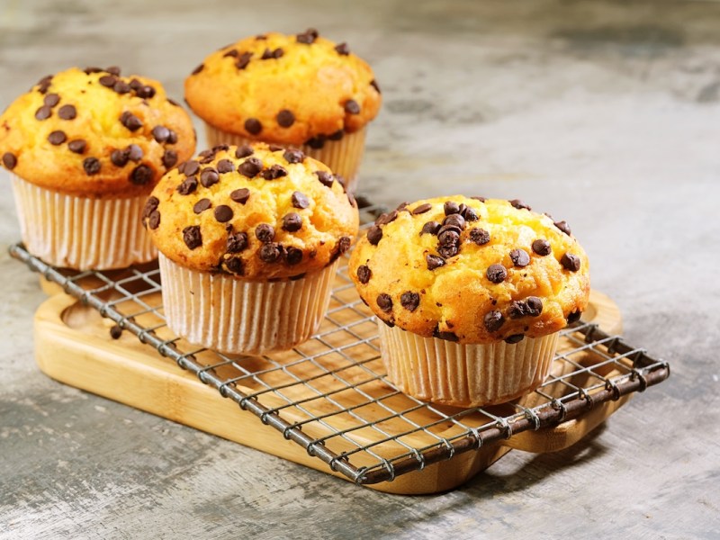 4 chocolate chip oat muffins on a wire rack placed on a wooden board.