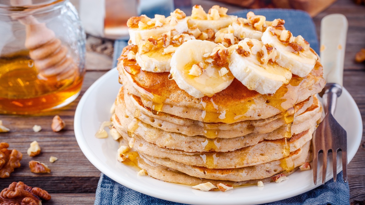 Pancakes on a white plate with banana, walnuts and syrup