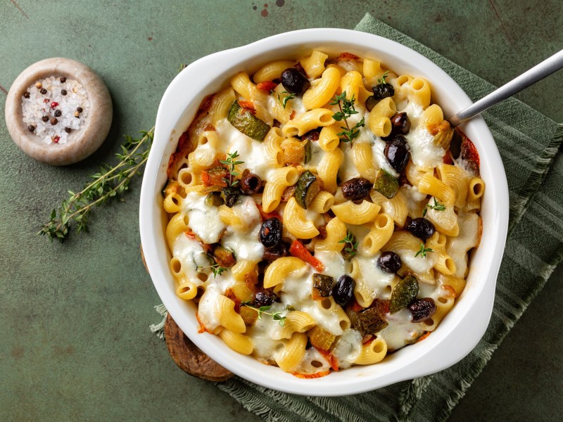 Mediterranean macaroni casserole in a white baking dish. Next to it is a pot of salt with peppercorns