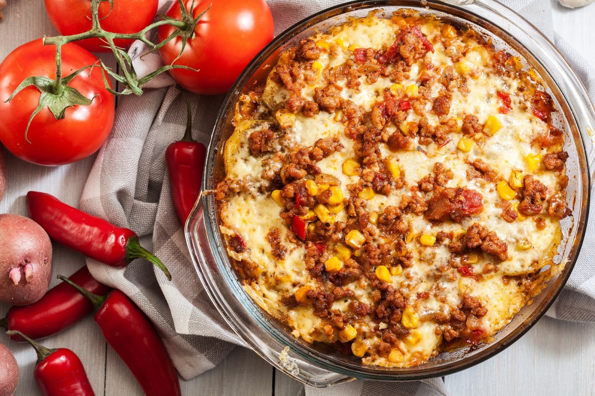 Mexican-style ground beef and potato casserole in a baking dish, next to tomatoes, chilies and potatoes.