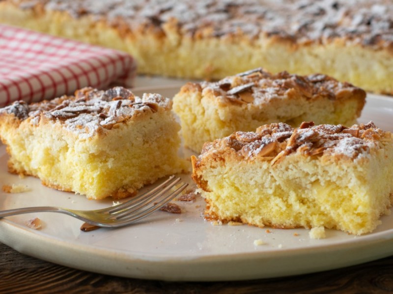 3 slices of no-yeast butter cake on a plate, in the background the sheet pan with the cake and a tea towel.