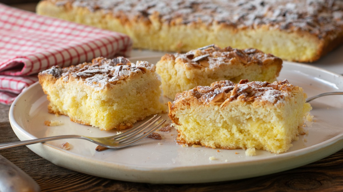 3 slices of no-yeast butter cake on a plate, in the background the sheet pan with the cake and a tea towel.