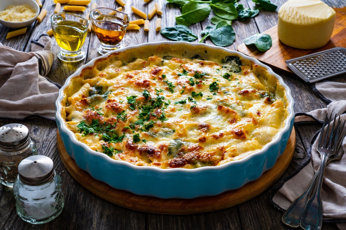 A round baking dish with pasta bake with feta and spinach, topped with cheese and sprinkled with parsley.