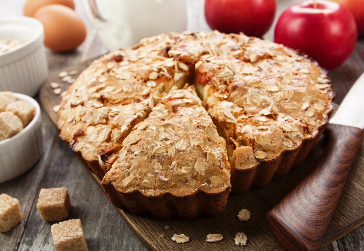Baking pan with apple-oatmeal cake on a table with apples next to it.