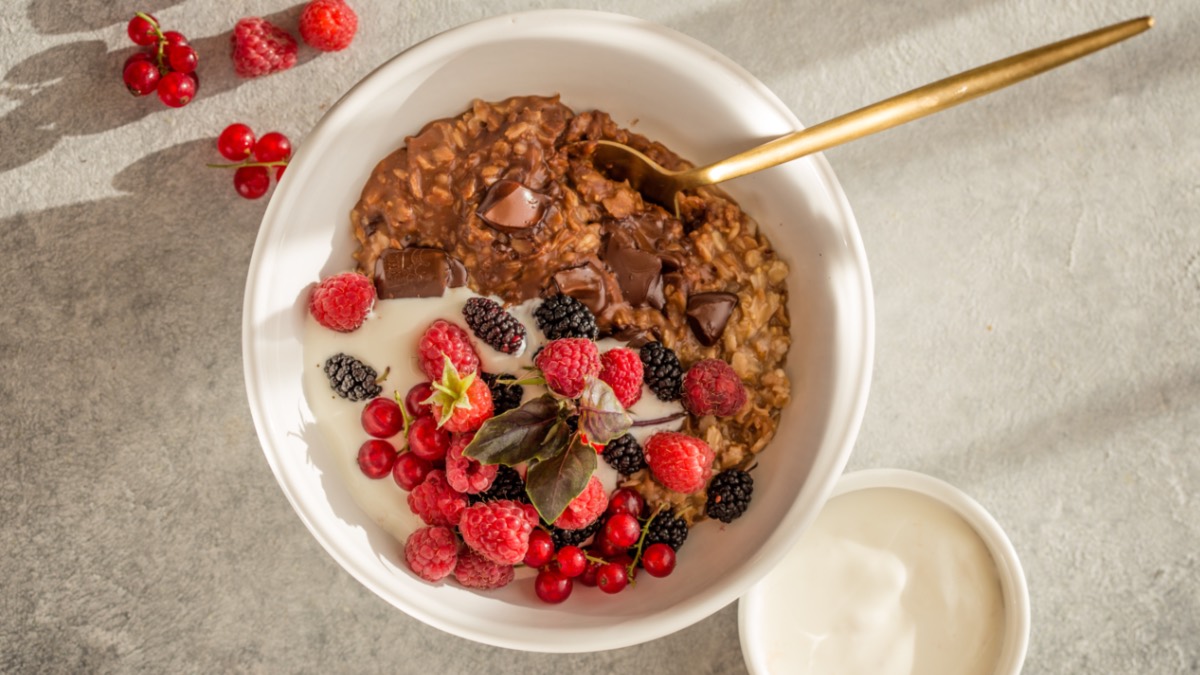 Chocolate oatmeal in a white bowl with fruit, top view.
