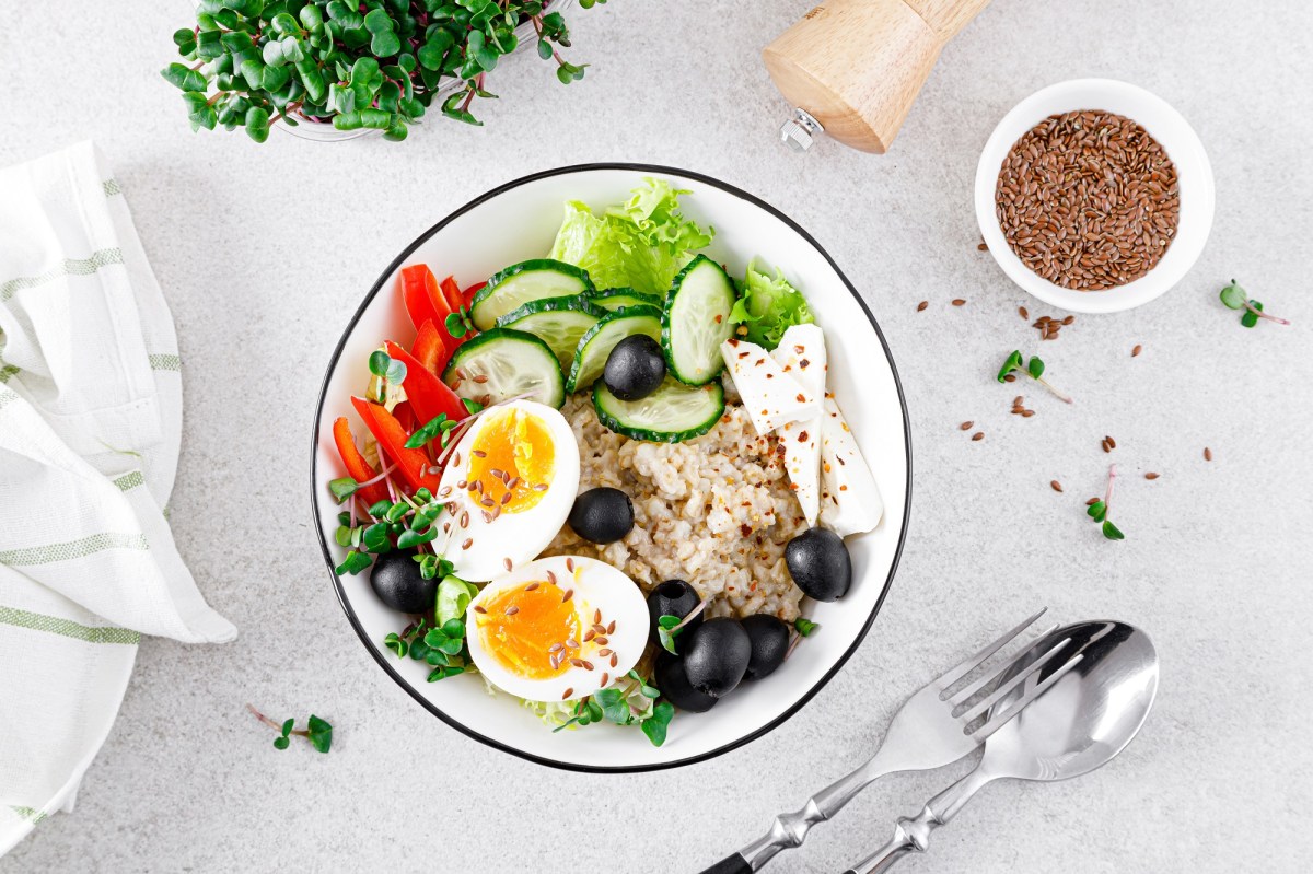 An oatmeal bowl with feta and egg, with bell peppers, lettuce, cucumbers, and olives.