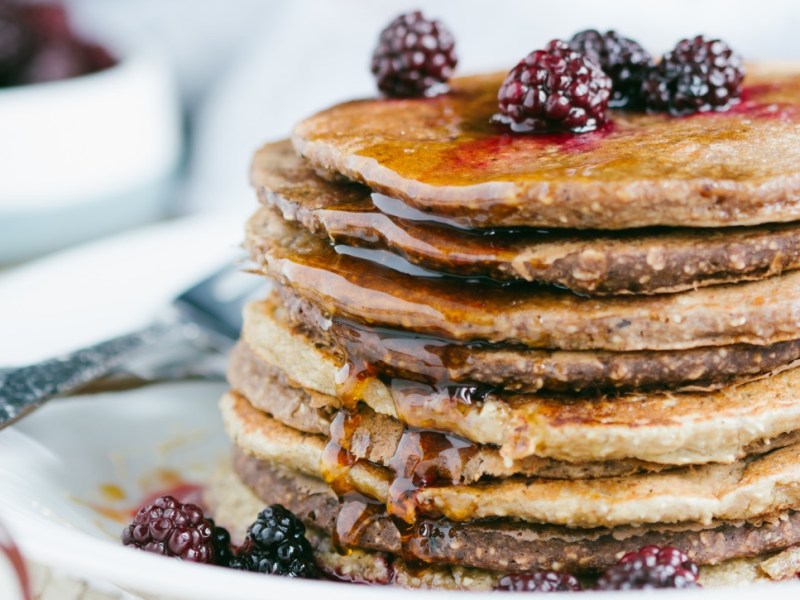 A stack of oatmeal pancakes with fresh blackberries and syrup.