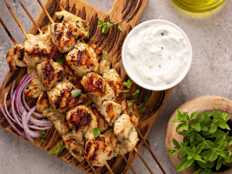 Several souvlaki. Next to them are onions and a bowl of tzatziki.
