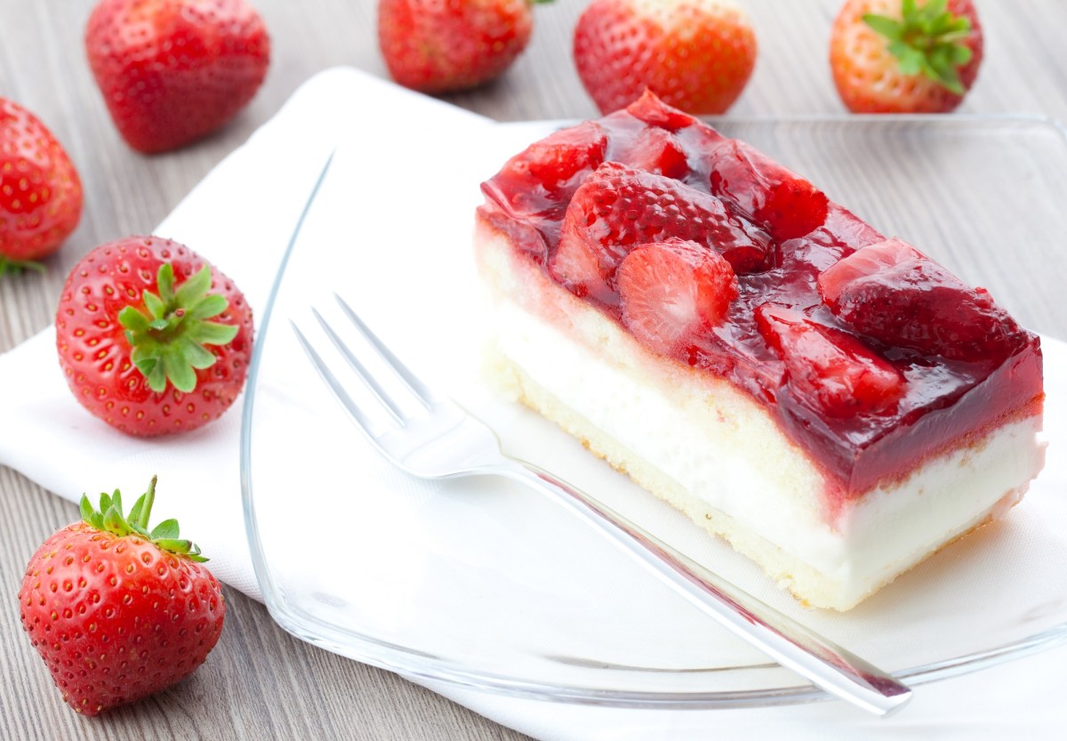 A piece of sheet pan strawberry cream cake on a plate, next to it a fork and fresh strawberries.