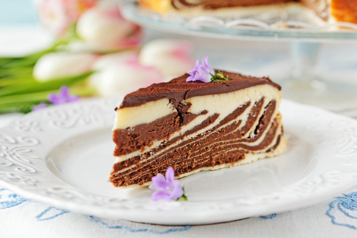 A slice of zebra cheesecake with light and dark batter on a plate, decorated with flowers.