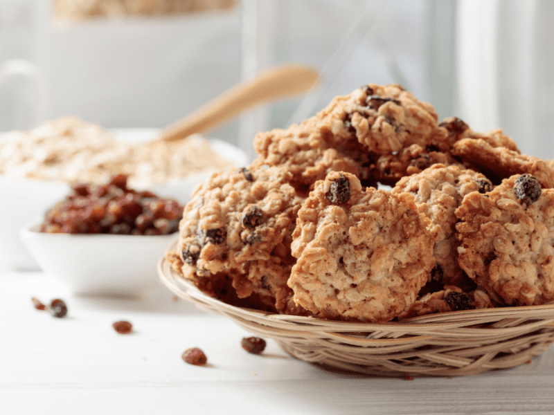 A few oat breakfast cookies rest on a round plate placed on a white table. The cookies have a golden-brown color and a textured surface, showing bits of oats and other ingredients. The white table and simple plate create a clean and inviting presentation.