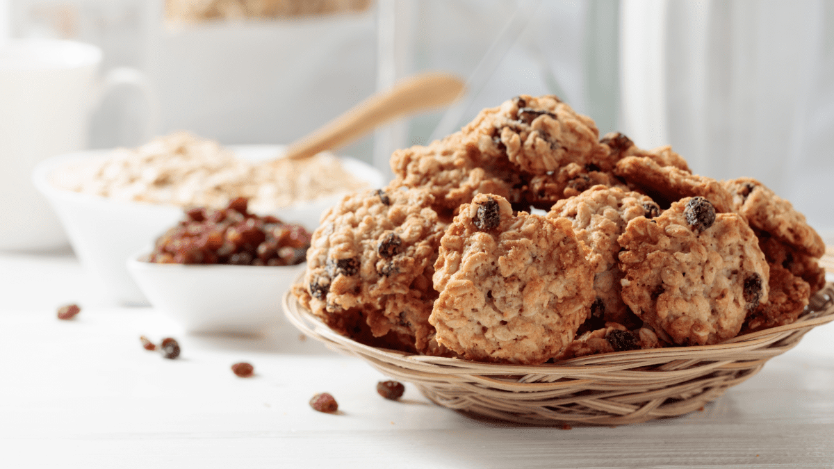 A few oat breakfast cookies rest on a round plate placed on a white table. The cookies have a golden-brown color and a textured surface, showing bits of oats and other ingredients. The white table and simple plate create a clean and inviting presentation.