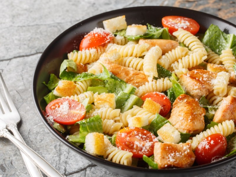 A plate of Caesar pasta salad with two forks next to it.