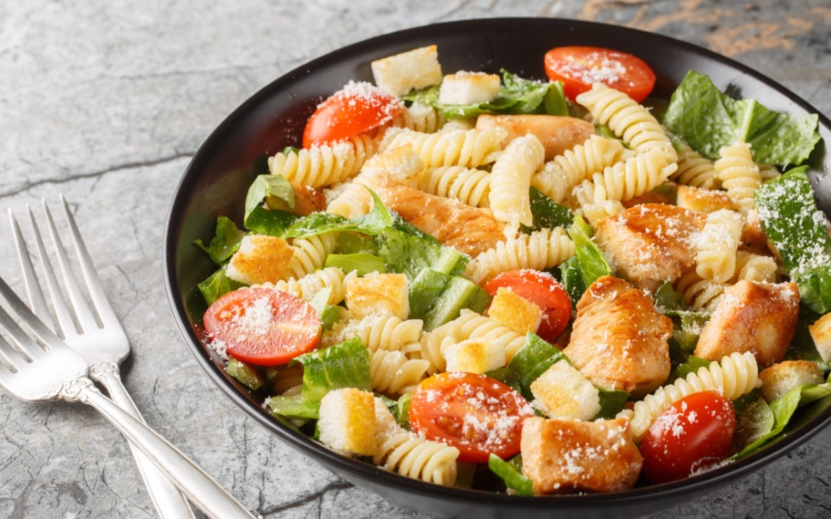 A plate of Caesar pasta salad with two forks next to it.