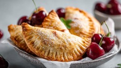 A bowl lined with white baking paper and freshly baked cherry empanadas from the air fryer. They are garnished with some fresh cherries.