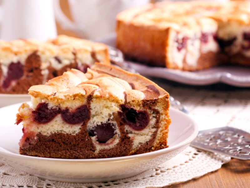 A piece of cherry filled marble cake on a plate. In the background, the rest of the cake and another piece on a plate can be seen.