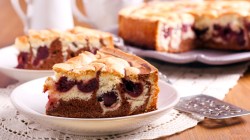 A piece of cherry filled marble cake on a plate. In the background, the rest of the cake and another piece on a plate can be seen.