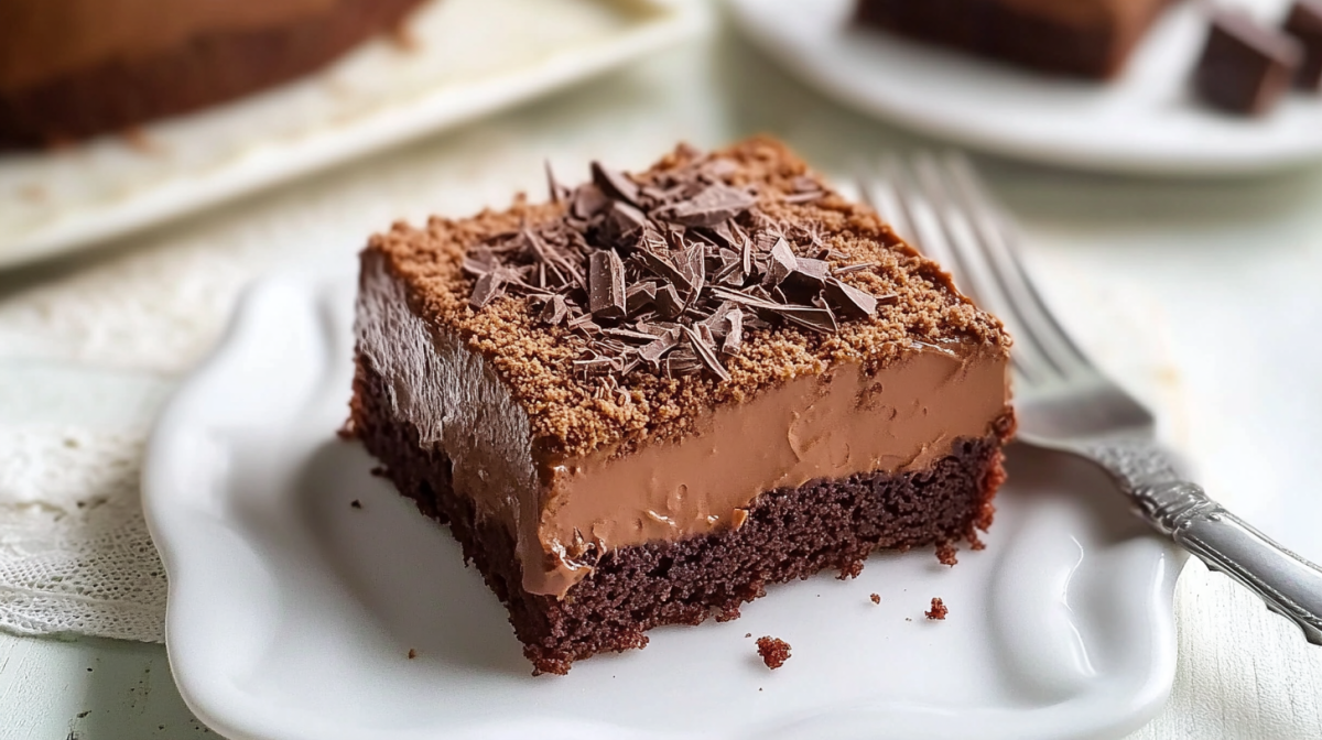 A piece of chocolate pudding sheet cake on a white plate. A fork lies next to it.