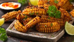A stack of corn ribs with parsley on a plate. Next to it is a bowl of dip.