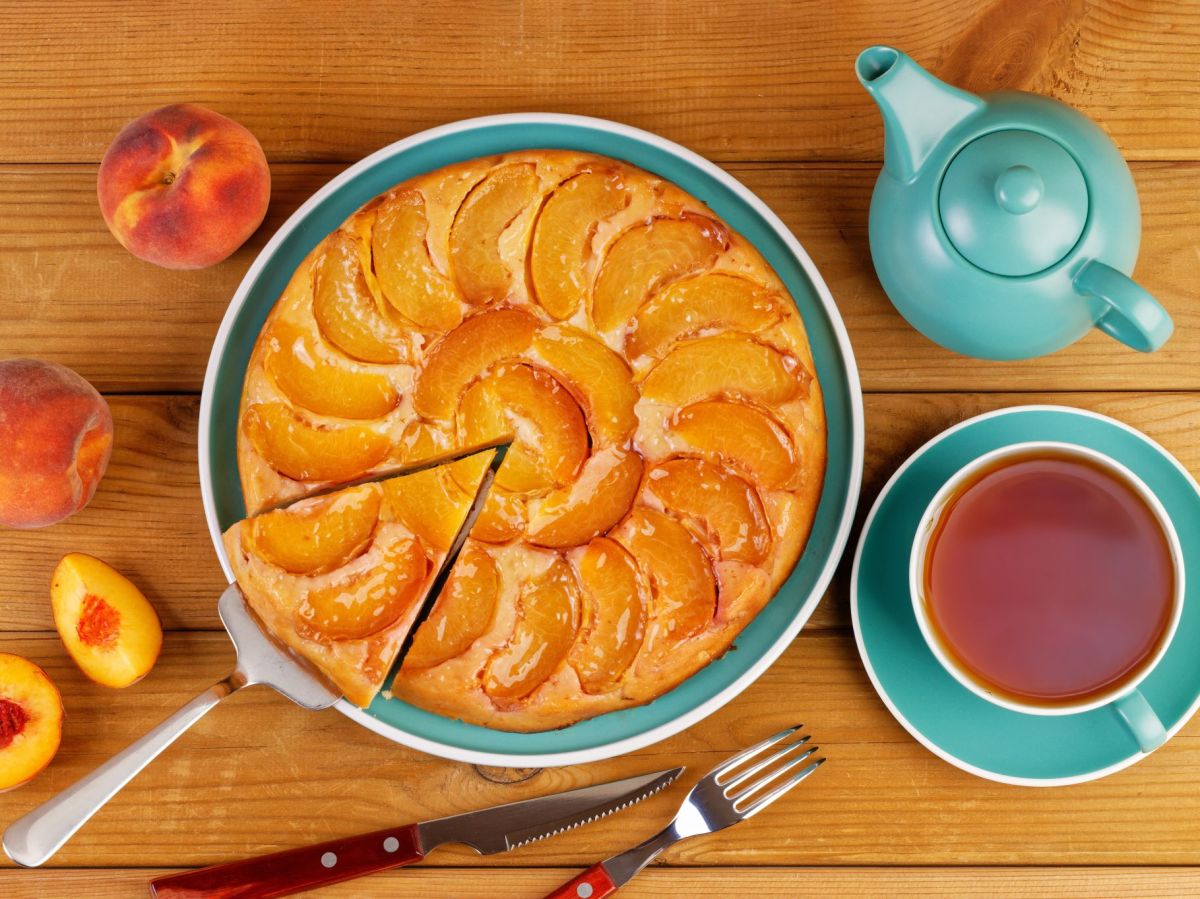 Easy peach cake, served on a pretty blue plate. Next to it are a blue coffee cup and a teapot. Peaches are placed next to it as decoration.
