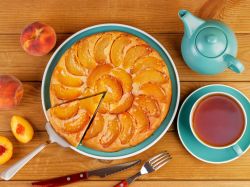 Easy peach cake, served on a pretty blue plate. Next to it are a blue coffee cup and a teapot. Peaches are placed next to it as decoration.