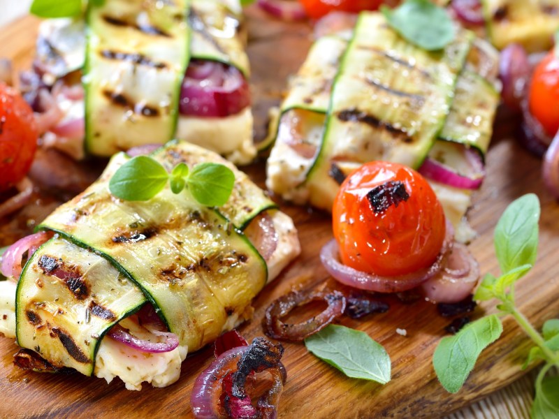 Wooden board with grilled feta and zucchini packets