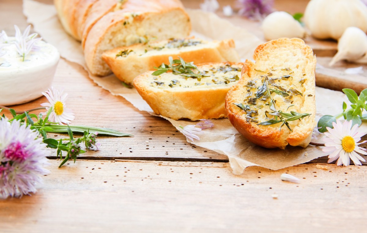 A sliced homemade herb baguette, next to fresh wildflowers