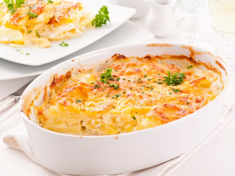Indian potato casserole in a baking dish, with a plate behind it holding a serving.
