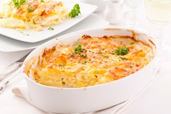 Indian potato casserole in a baking dish, with a plate behind it holding a serving.