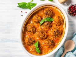 Lentil balls in coconut curry sauce in a baking dish. Spices, a cooking spoon, and a cloth napkin lie next to it as decoration.