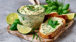 Lime-basil butter, served in a small glass. Next to it is a slice of bread with the butter. Limes and basil as decoration next to it.