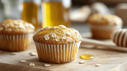 A golden honey oat muffin on a wooden block with honey behind it.