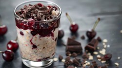 A clear jar filled with oats chocolates and cherries sits on a gray table.