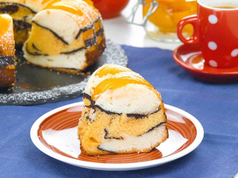 A slice of peach cake with cocoa in a wave pattern on a plate.