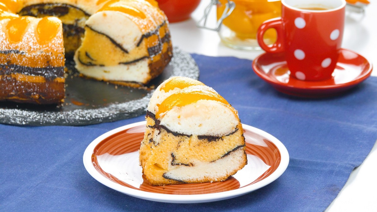 A slice of peach cake with cocoa in a wave pattern on a plate.