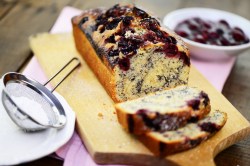 Sliced poppy seed cake with cherries on a wooden board