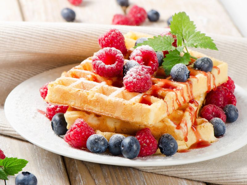 Fanta cake waffles, stacked on a plate. Fresh berries and a mint leaf serve as decoration.