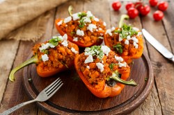 Four halves of grilled stuffed bell peppers lie on a wooden board. Cutlery lies next to it.