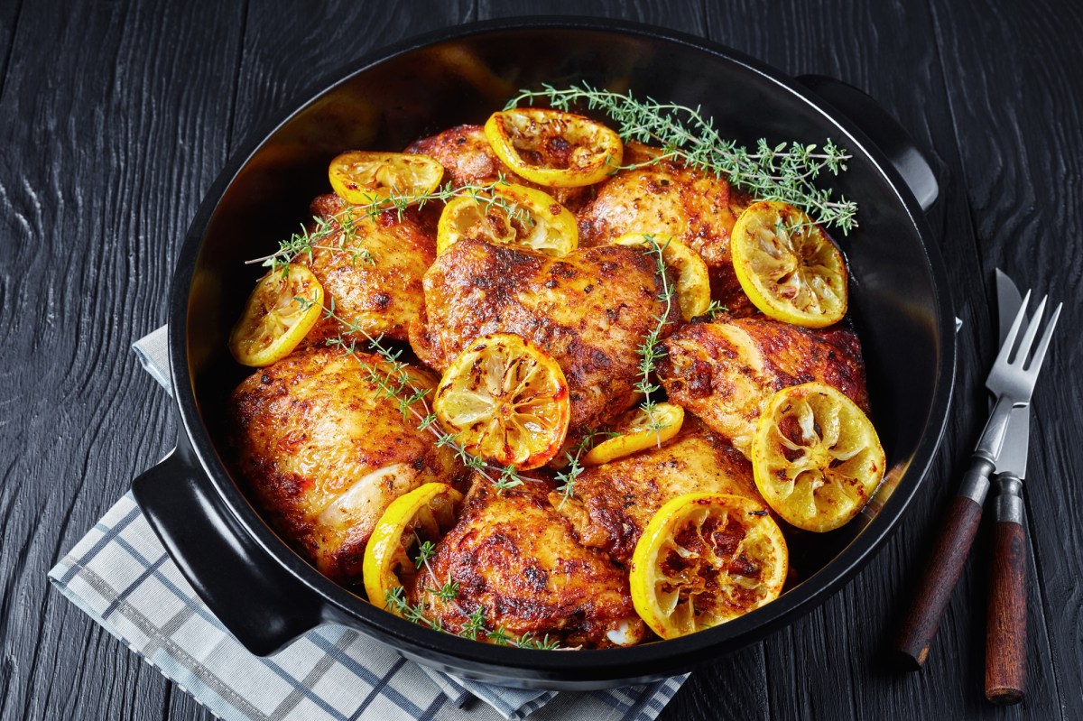 Lemon roasted chicken in a cast iron pan with lemon slices.