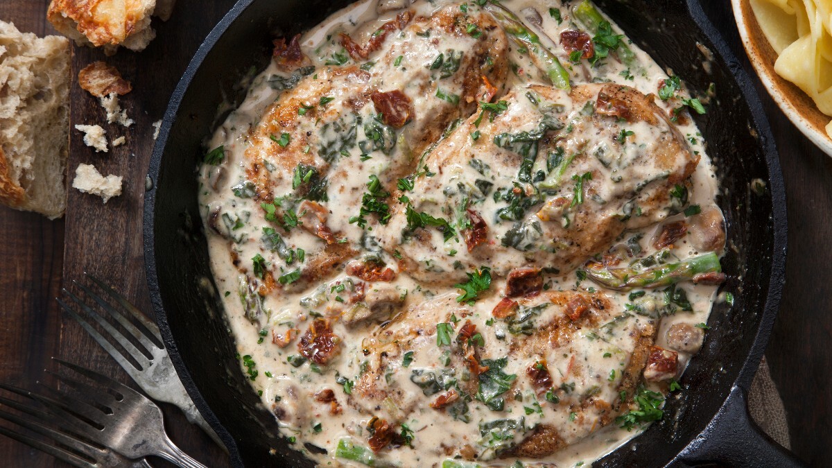 Chicken in parmesan sauce in a pan, photographed from above. Beside it are cutlery and breadcrumbs.