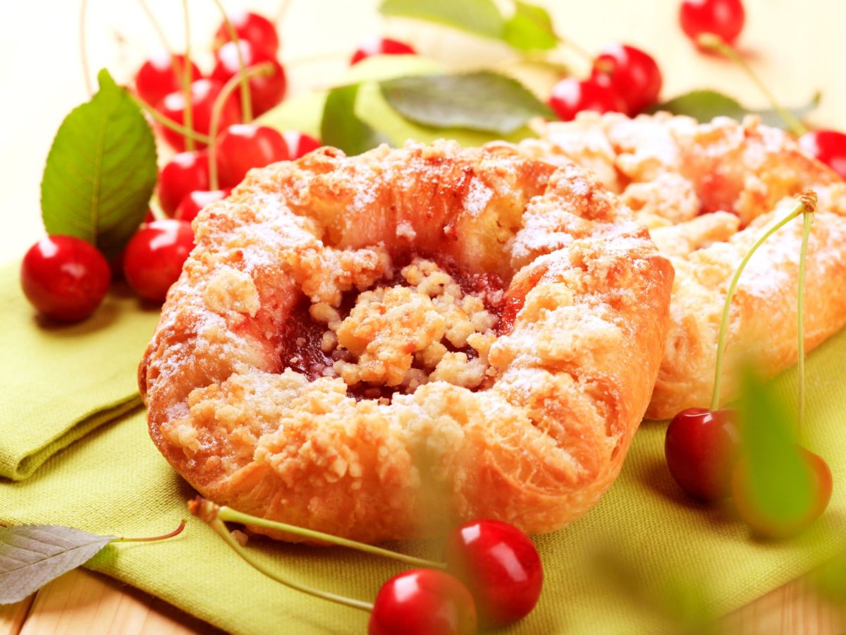 Puff pastry streusel squares lie on a board. Cherries are scattered around as decoration.