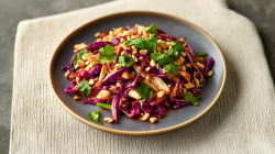 A plate of red cabbage salad with chicken garnished with chopped peanuts and fresh cilantro. The plate is on a cream-colored placemat.