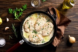 Rosemary chicken in a pan on a brown cloth, surrounded by herbs and onions.