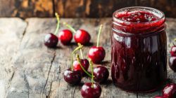 A jar of sour cherry jam, with sour cherries in the background and next to it.