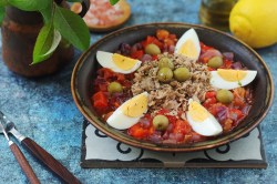 Tunisian grilled salad Slata Mechouia, served with tuna and eggs, on a dark plate.