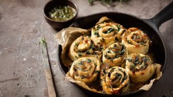 A deep cast iron pan with vegan spinach rolls. Next to it is a thin knife. There is also a small bowl of liquid garlic butter next to it.