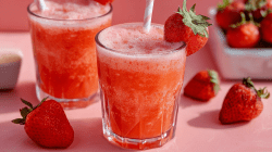 Two glasses of strawberry gin fizz with straws. Individual strawberries lie around as decoration.