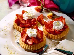 3 strawberry tarts with vanilla cream on a plate, decorated with chopped pistachios.