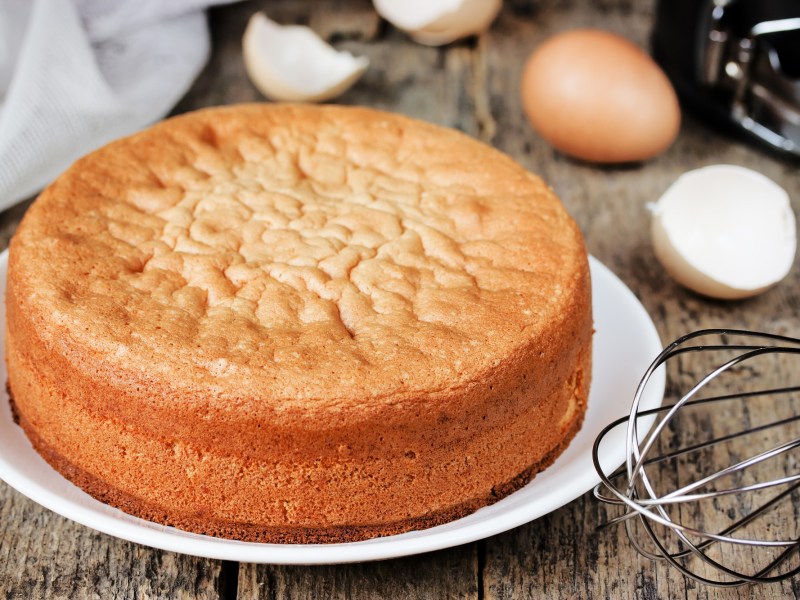 Two-ingredient marzipan cake on a white plate. Behind it are eggshells and a whisk.