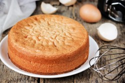 Two-ingredient marzipan cake on a white plate. Behind it are eggshells and a whisk.